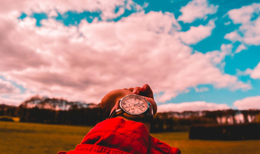 Close-up of a wristwatch with a scenic background of a field and cloudy sky.