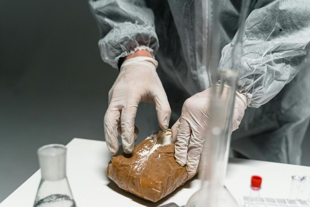 Lab worker analyzes powdered substance in a laboratory setting using safety gear.